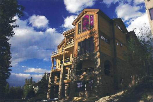 A timber and stone mountain home with tall windows and stacked balconies overlooking a wooded mountain landscape in Breckenridge, Colorado