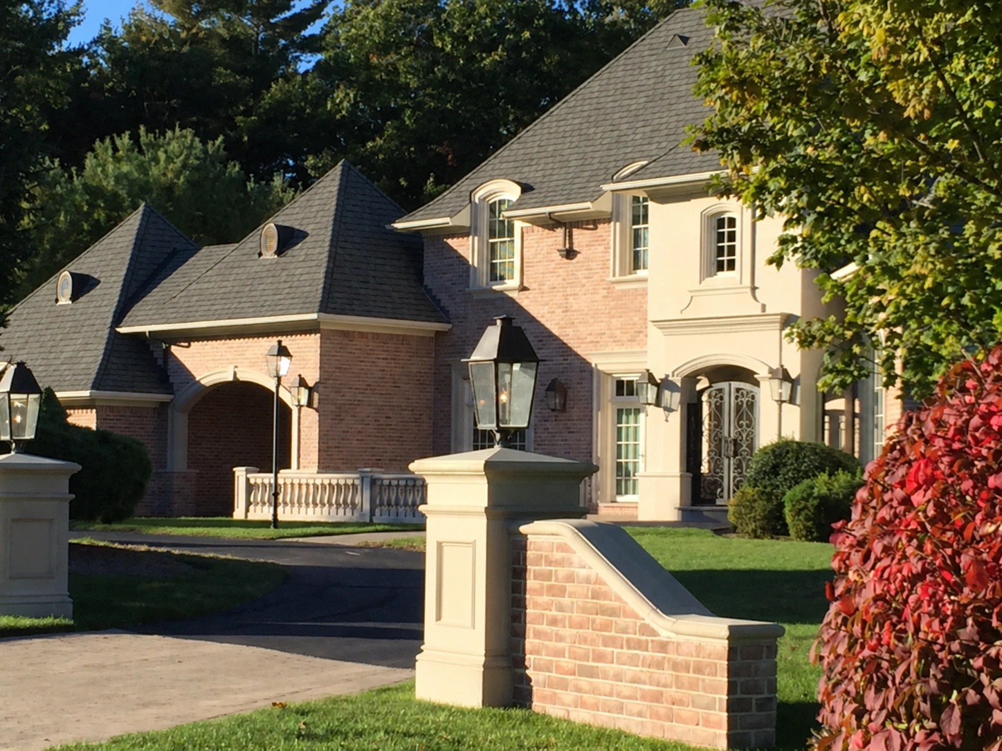 A brick and stone residence framed by mature trees and a landscaped garden approach